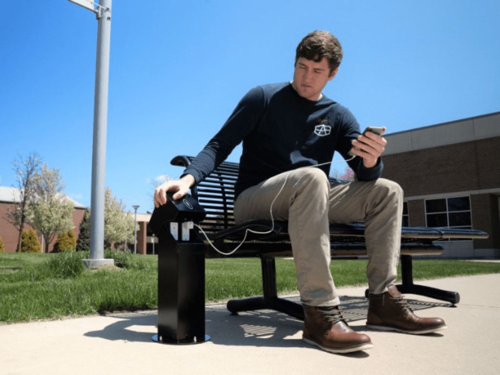 Man charging phone using Pedoc power pedestal on college campus